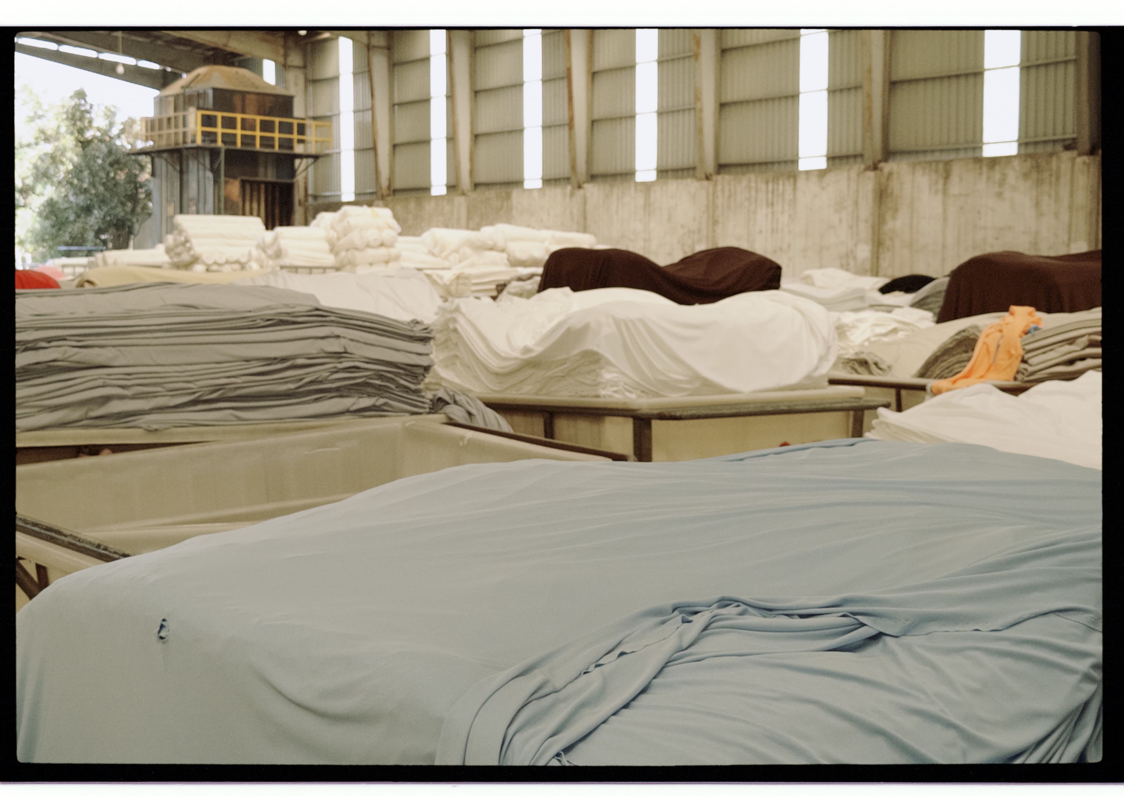 Stacks of pale blue, gray, and white fabric in containers across a dyehouse workshop.